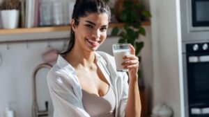 Un adulto sosteniendo un vaso de leche en la cocina: La leche es esencial para mantener la densidad ósea y prevenir la pérdida de masa ósea en la adultez, gracias a su alto contenido de calcio.