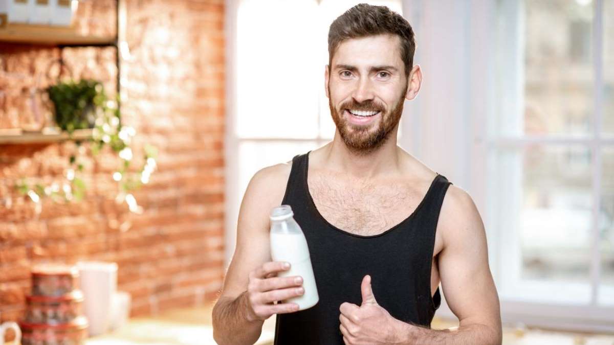 Un hombre sostiene una botella de leche, destacando su composición como emulsión de lípidos, proteínas, carbohidratos y minerales, esenciales para la nutrición y el desarrollo.