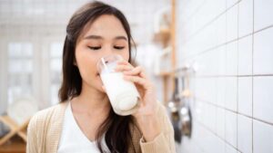 Un adulto disfruta de un vaso de leche en la cocina, destacando cómo este alimento esencial ayuda a mantener la masa muscular y ósea.