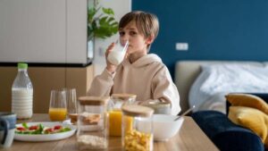 Un niño disfruta de un vaso de leche durante el desayuno, destacando la importancia de este alimento en la infancia para el desarrollo de huesos y dientes fuertes.