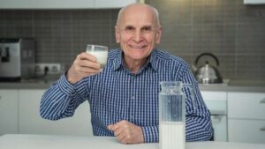 Un hombre mayor con un vaso de leche en la mano, simboliza los efectos positivos de los lácteos en la microbiota intestinal, incluyendo la promoción de bacterias probióticas que regulan el pH intestinal y mejoran la absorción de minerales.